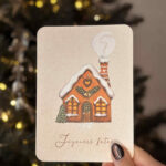 Carte de vœux illustrée représentant une maison pain d’épices enneigée et décorée pour Noël.
