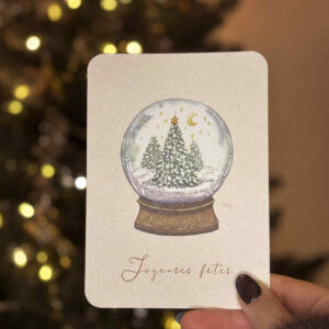 Carte de vœux illustrée représentant une boule à neige contenant des sapins enneigés et des étoiles dorées.