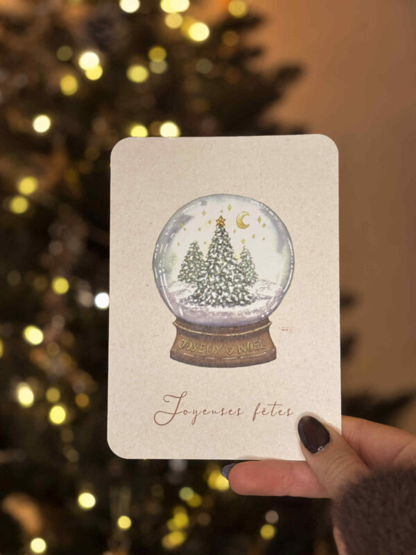 Carte de vœux illustrée représentant une boule à neige contenant des sapins enneigés et des étoiles dorées.