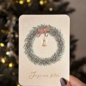 Carte illustrée représentant une couronne de Noël en sapin, décorée de baies rouges, d’un nœud en satin et d’un petit ange en bois.